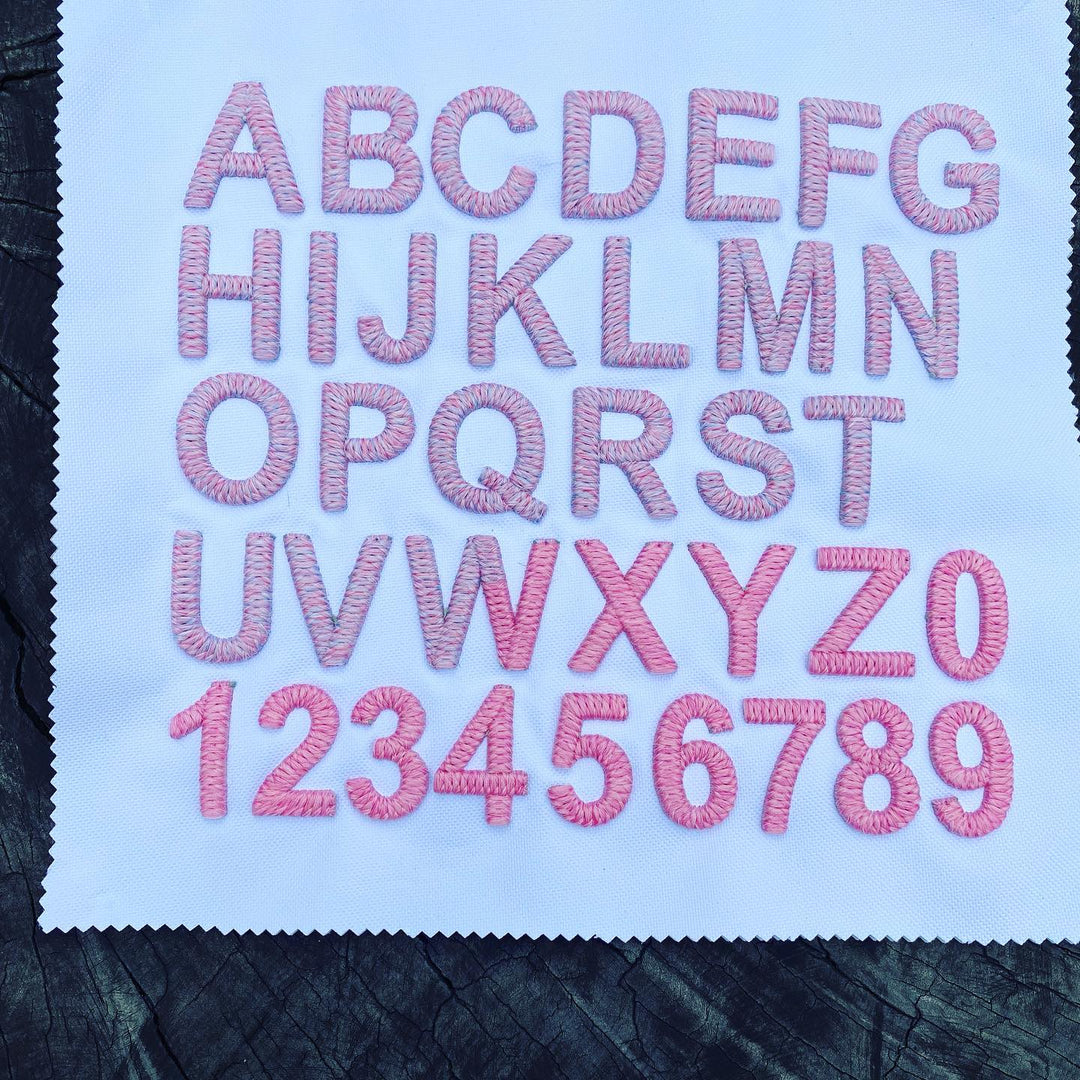 Embroidered letters and numbers on a fabric swatch with pink thread.