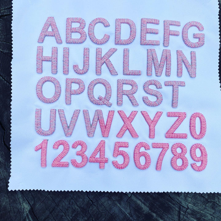 Embroidered letters and numbers on a fabric swatch with pink thread.