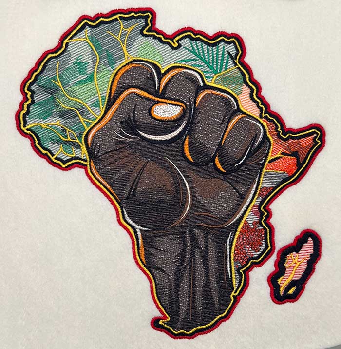 Embroidered featuring a map of the African continent with a raised fist symbol in the center, surrounded by Adinkra symbols and patterns.