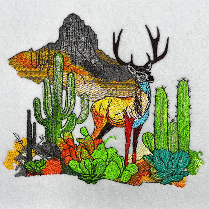 Embroidered sweatshirt with a design of a mountain deer among snow-dusted pines and wild flowers.