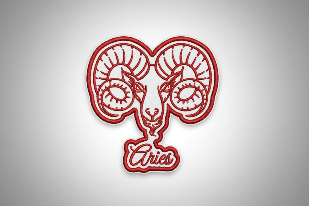  Red Aries ram head zodiac embroidered patch with curled horns and “Aries” script text on a white grid background.