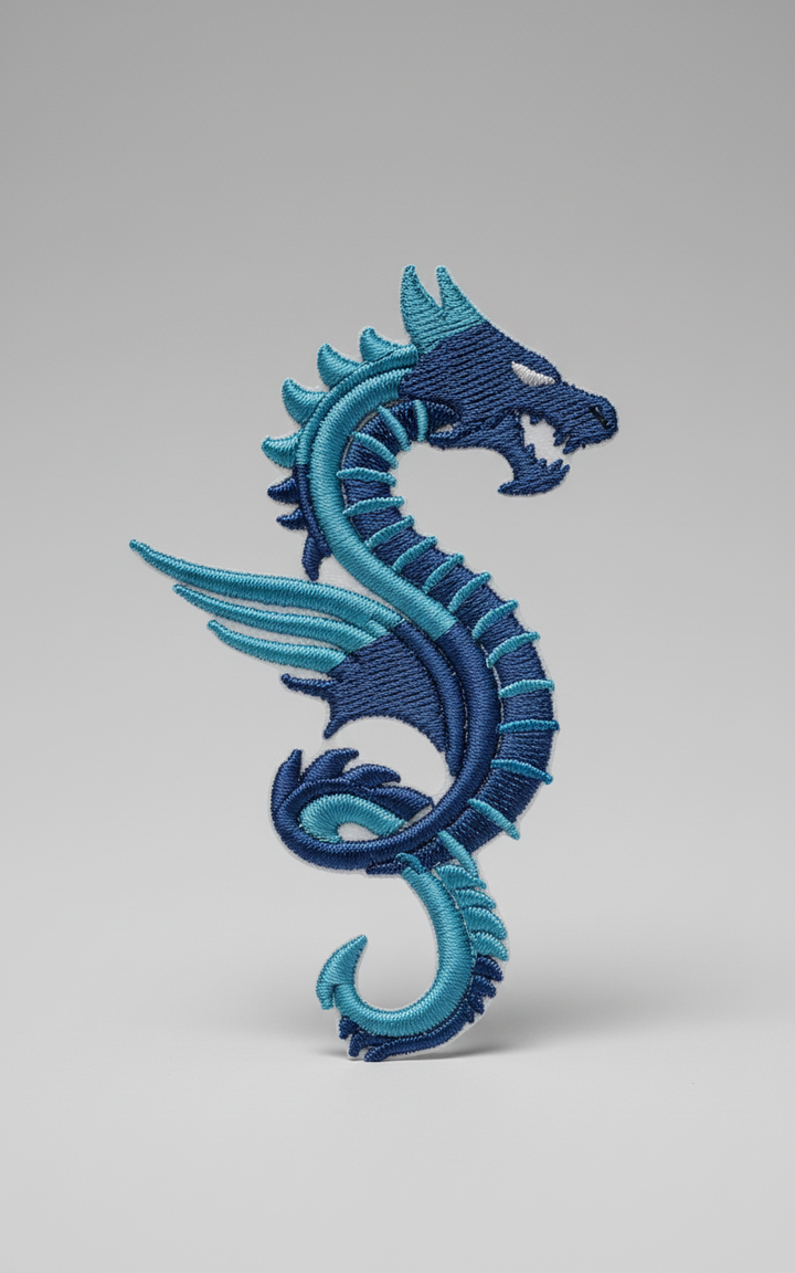 Blue winged dragon embroidery patch featuring a sleek serpentine dragon with small wings and spiked back, stitched in navy and teal tones with layered thread texture on a light background, original EmbroMania artwork.