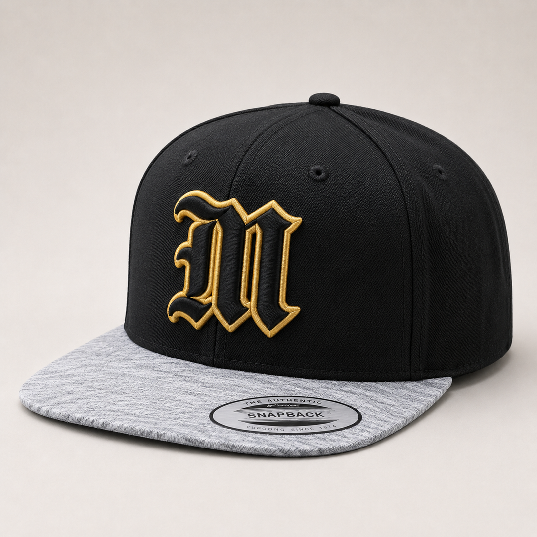 Black and gray snapback cap with gold logo on a light gray background