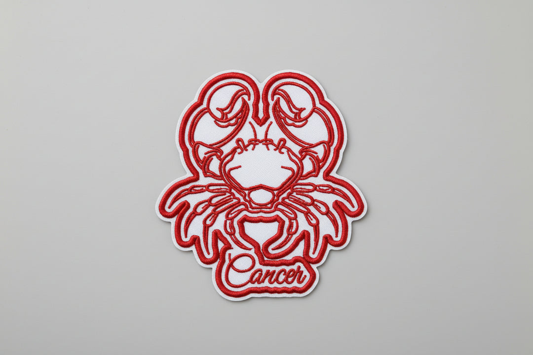 Cancer zodiac crab embroidery patch featuring a stylized crab with claws and legs in red outline stitching and the word “Cancer” in script below, on a light background, original EmbroMania artwork.