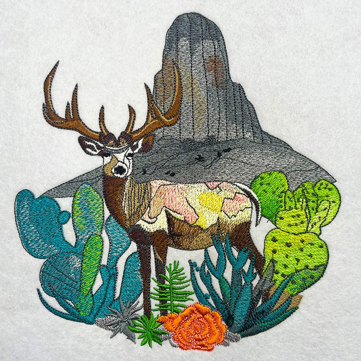 Embroidered  design of a mountain deer surrounded by wildflowers and alpine pines against a rainbow-colored background.