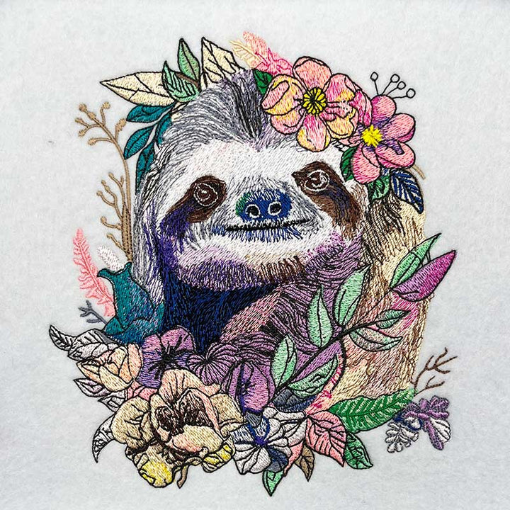 Embroidered design of a sloth surrounded by flowers and leaves on a white background