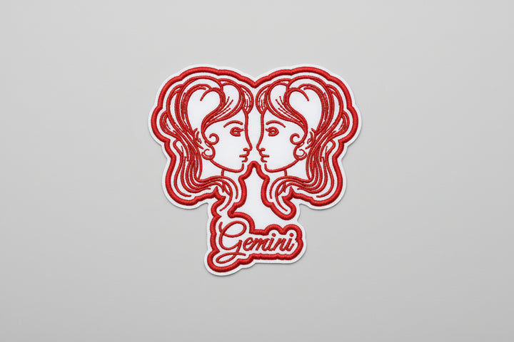 Gemini zodiac twins embroidery patch featuring two mirrored twin faces in red outline stitching and the word “Gemini” in script below, on a light background, original EmbroMania artwork.