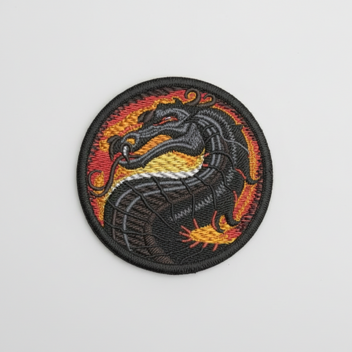 Round dragon emblem embroidery patch featuring a black dragon head with red and gold flame background inside a circular black border, stitched with detailed thread texture on a light background, original EmbroMania artwork.