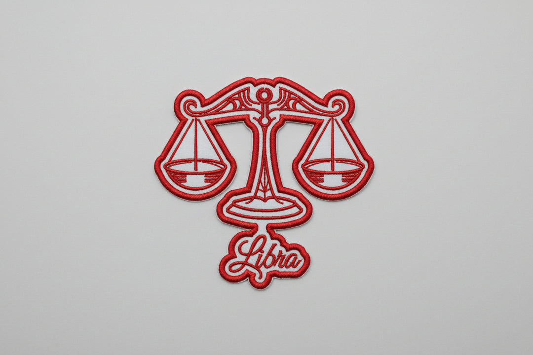 Red Libra scales zodiac embroidered patch with “Libra” script text on a white grid background.