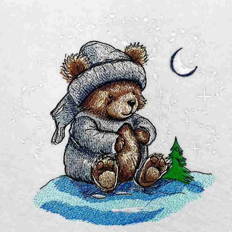 Embroidered design of a teddy bear wearing a winter hat and coat, sitting on snow with a small tree and crescent moon in the background.