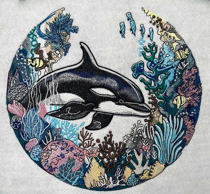 Embroidered jute tote bag featuring an orca whale and coral reef design with blue, green, and brown colors.