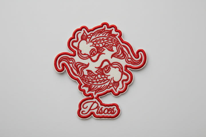 Pisces zodiac fish embroidery patch featuring two stylized fish circling in red outline stitching and the word “Pisces” in script below, on a light background, original EmbroMania artwork.
