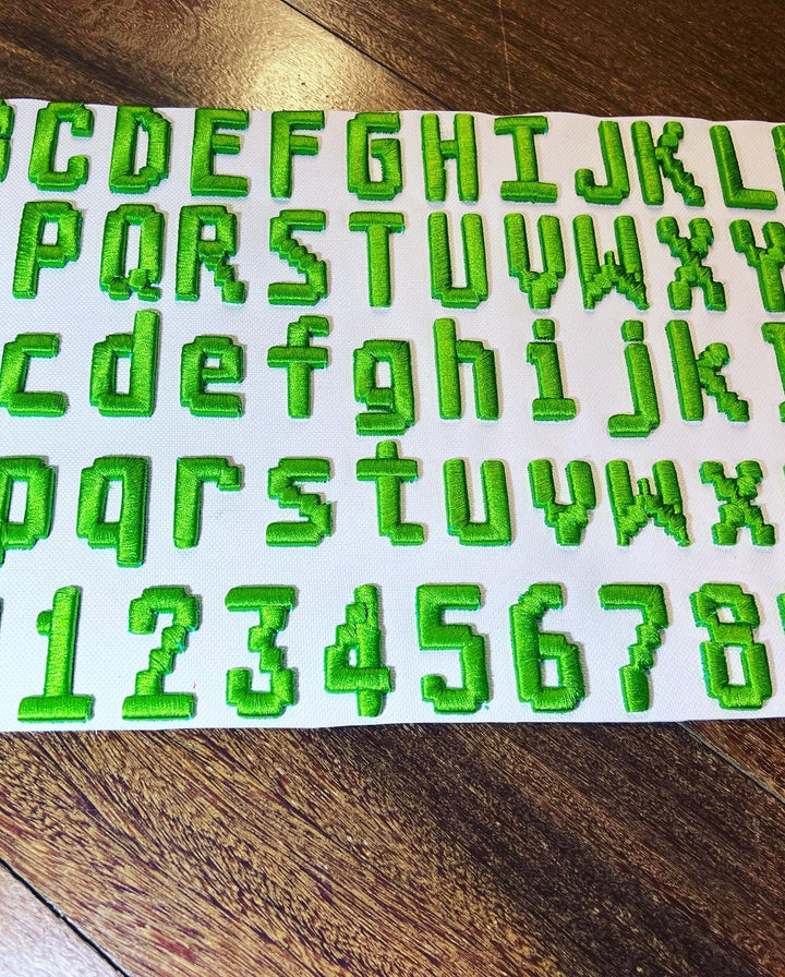 Sheet of green embroidered letters and numbers on a wooden surface