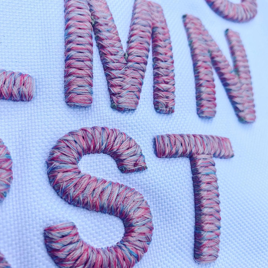 Colorful yarn letters spelling 'WONST' on a textured white background