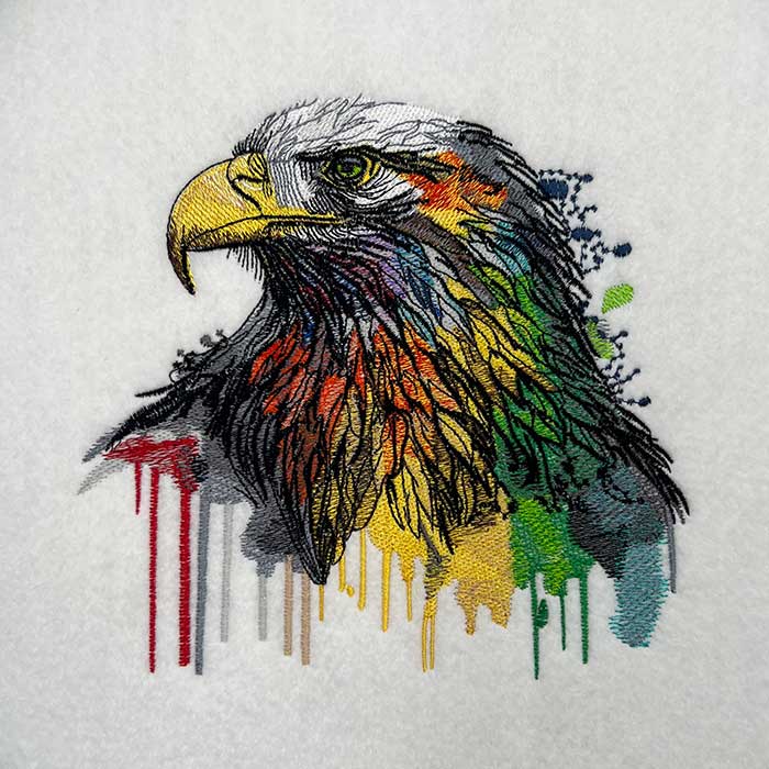 A colorful embroidered depiction of an eagle on a white jute tote bag.
