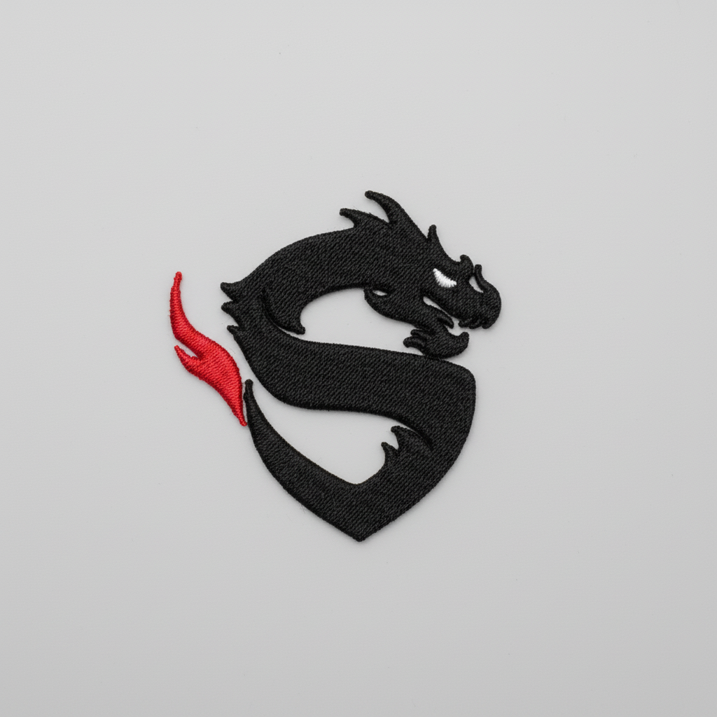 Minimal dragon embroidery patch featuring a black dragon silhouette with a sharp white eye and a red flame accent on the tail, stitched on a light background, original EmbroMania artwork.