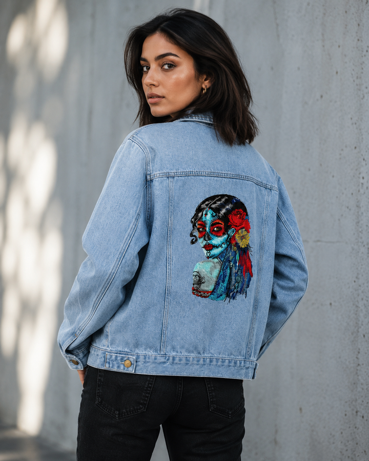 Woman wearing a denim jacket with a colorful graphic on the back against a gray wall.