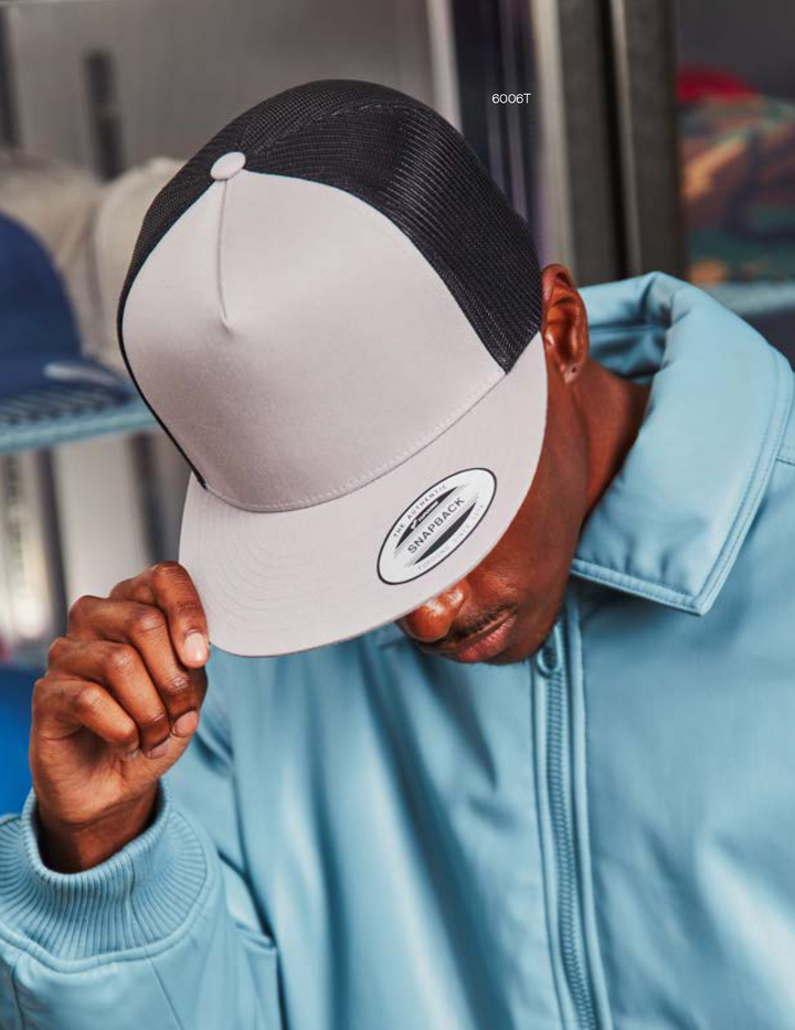 A person wearing a gray and black YP Classics trucker cap with a white front panel, from the 6006 Collection.