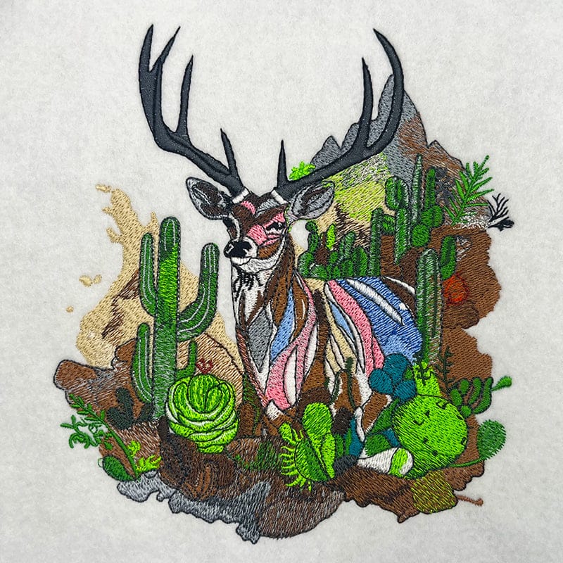 Short behind-the-scenes video showing an embroidery machine stitching a colorful deer with antlers in a desert cactus landscape, ending with EmbroMania branding.