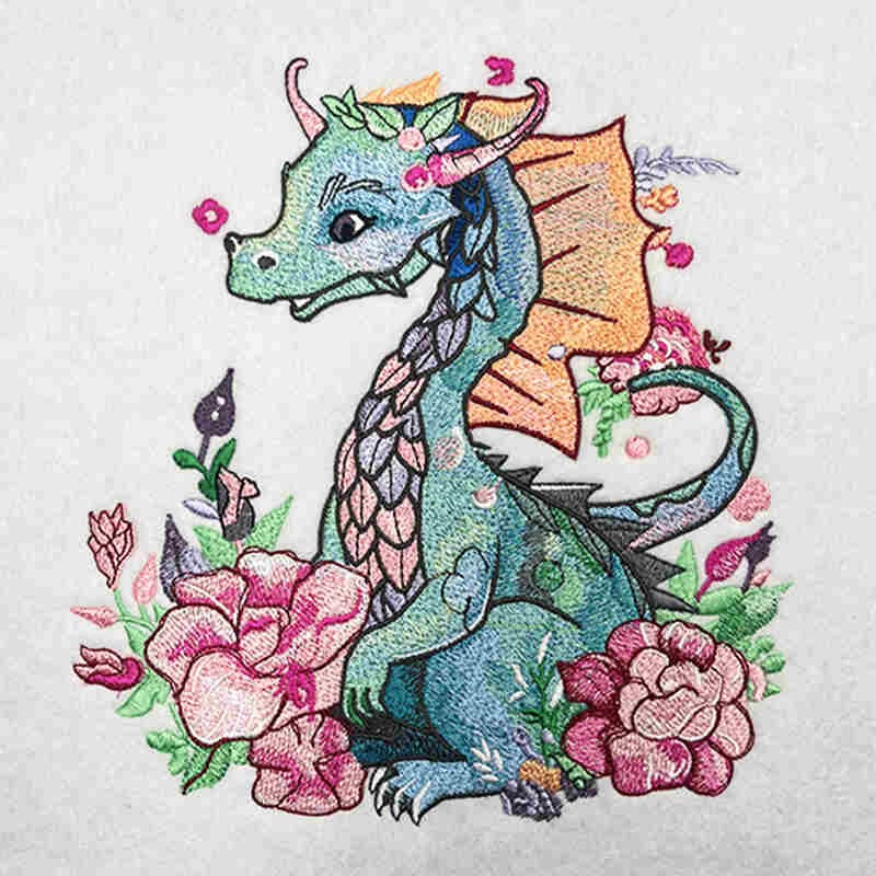 Close-up of an embroidered teal dragon with orange wings surrounded by pink flowers on a light fabric background.